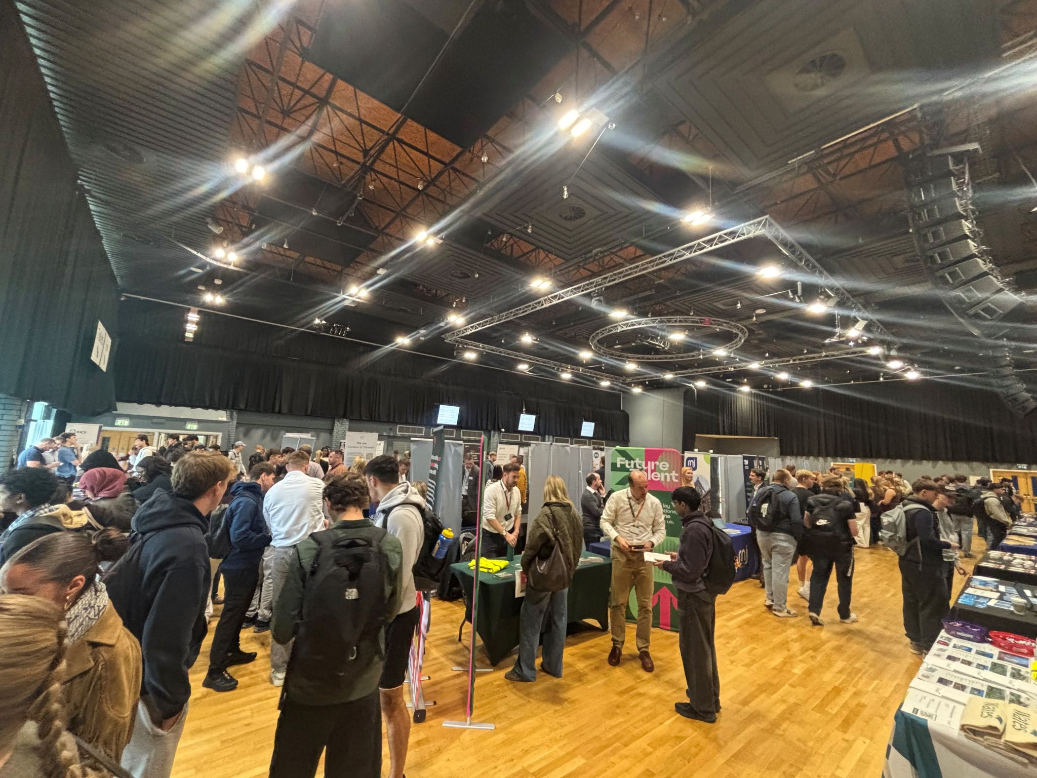 Students speaking with exhibitors among the careers fair stands in the university hall