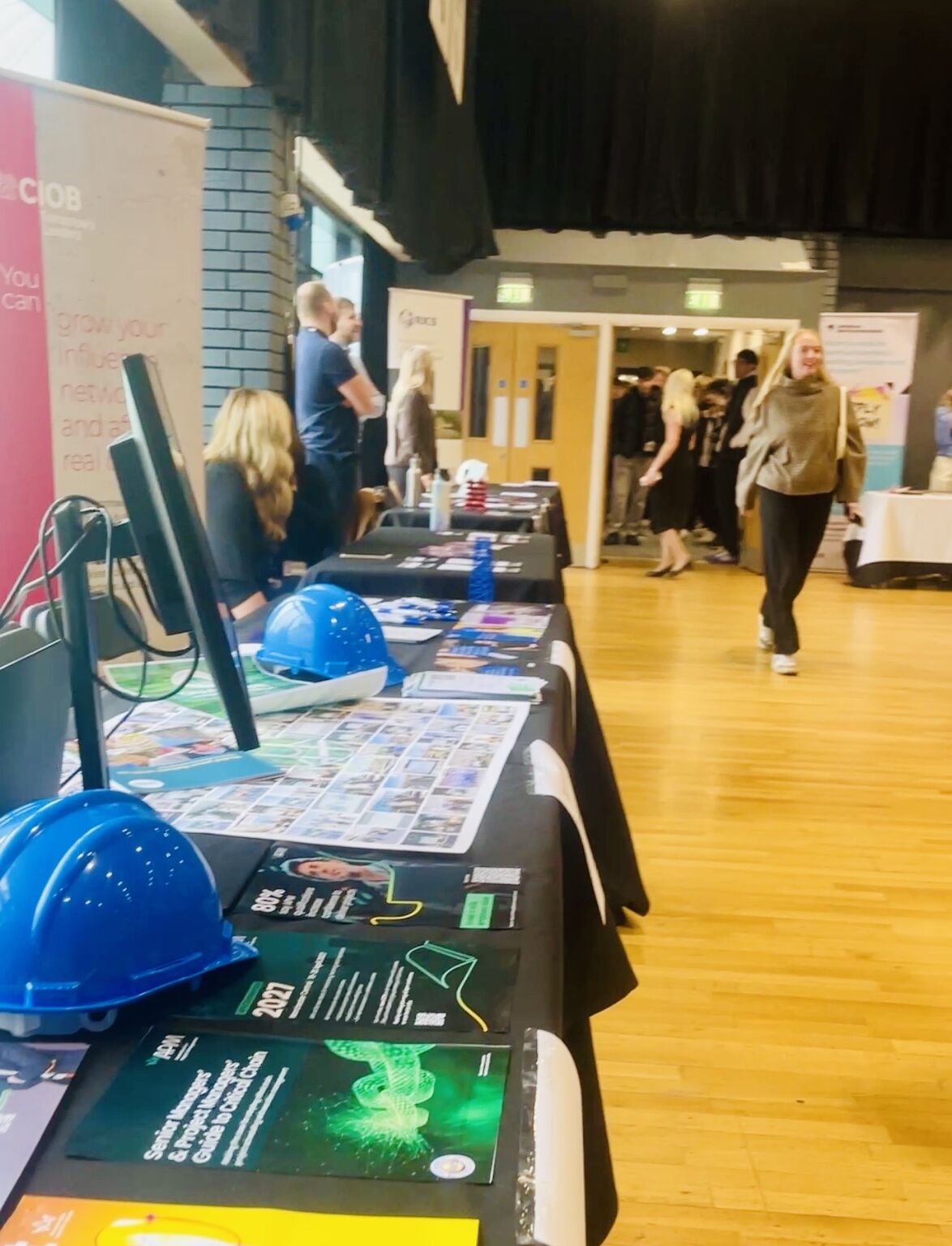 A row of careers fair stands displaying printed resources and blue hard hats