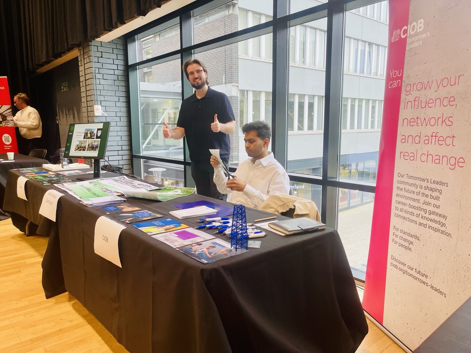 Representatives behind a stand displaying professional membership literature beside a CIOB banner